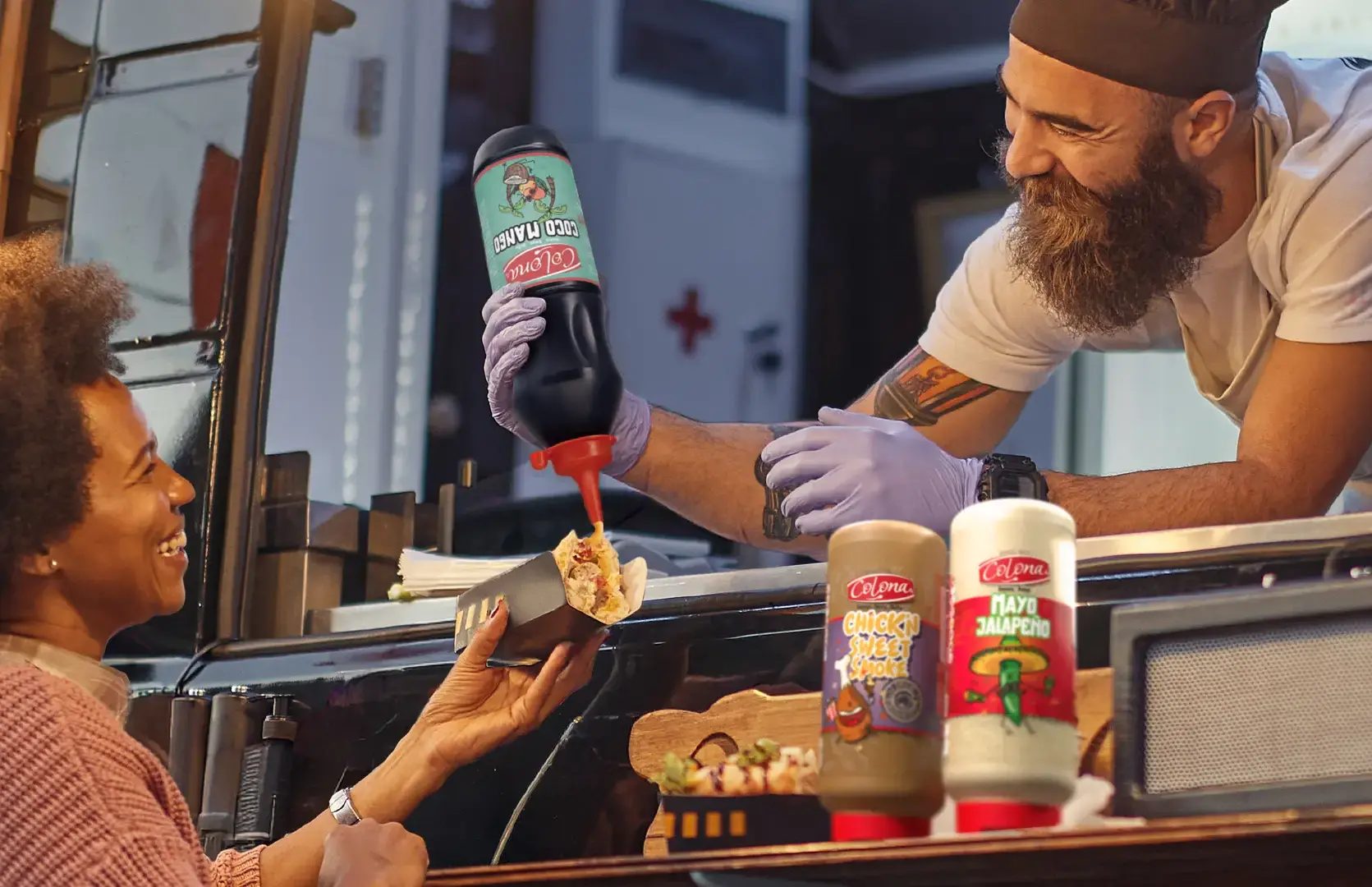 vente de street food depuis un food truck, le cuisinier sauce le hot dog de la cliente avec de la sauce Coco Mango de Colona, il vend aussi de la Chick'n Sweet Smoke de Colona et de la Mayo Japaleno de Colona